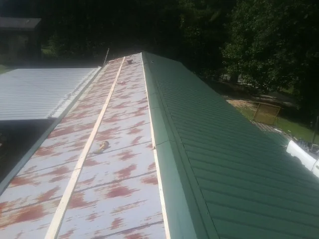 Old rusted panels beside newly installed green metal roofing — Wind Damage Roof Repair by Roofing Brothers in Braddock Heights
