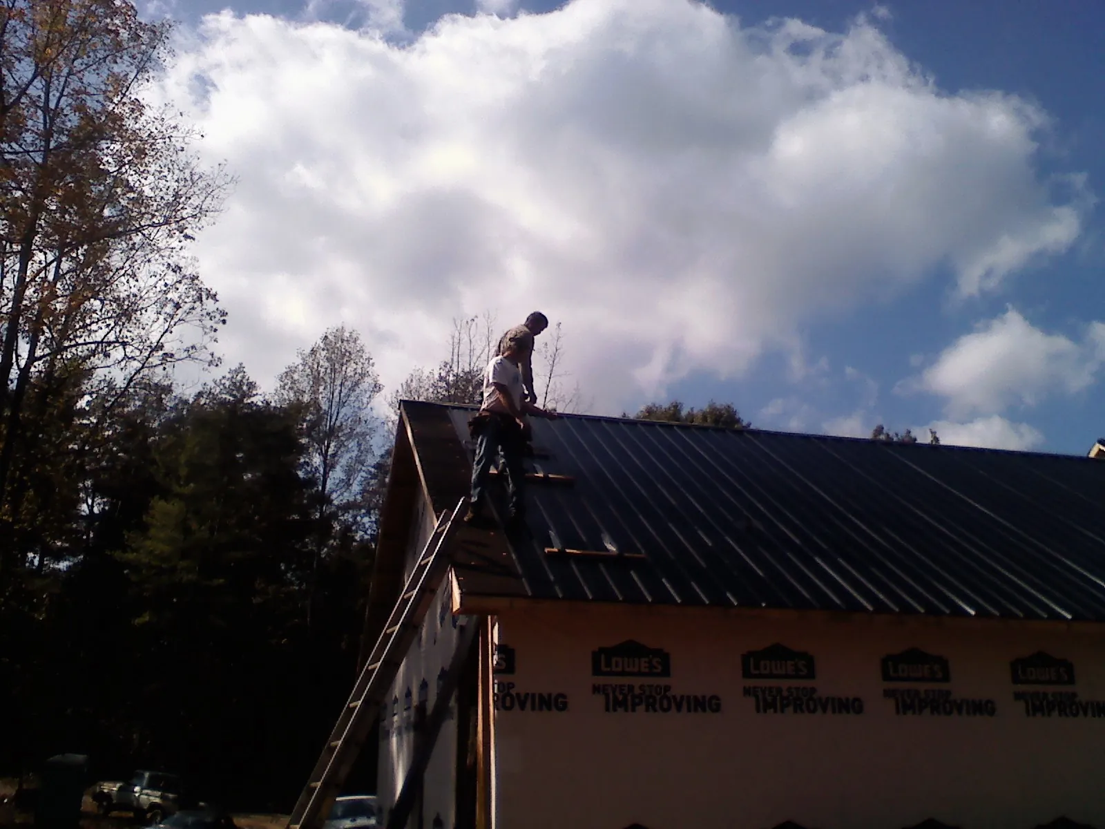 Roofer fastening dark metal panels high against a cloudy sky, from a Roof Inspection job in Braddock Heights