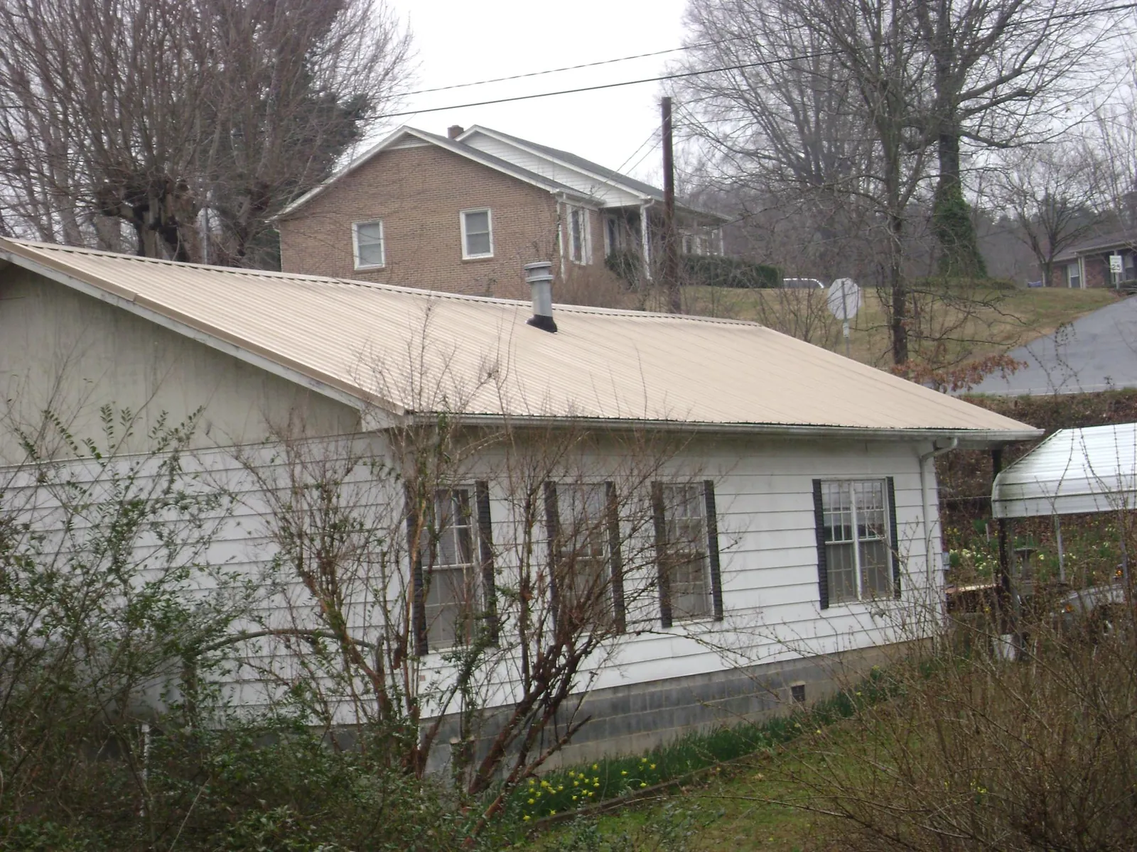 Tan metal roof on a white sided house set into a hillside — Commercial Roofing by Roofing Brothers in Braddock Heights